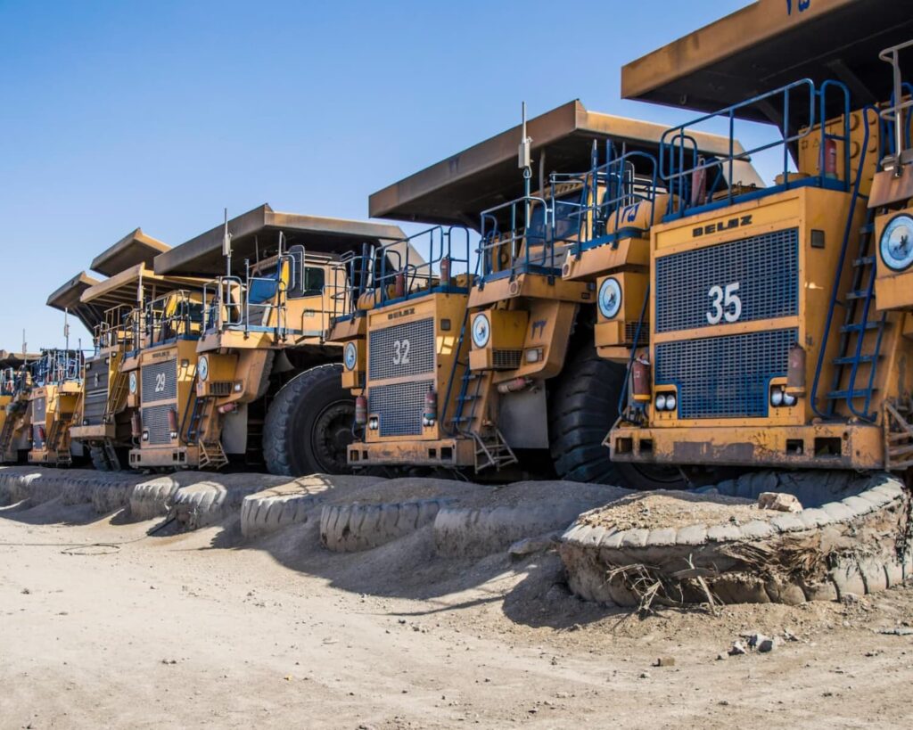 A group of dumper trucks parked in one row out on a site.